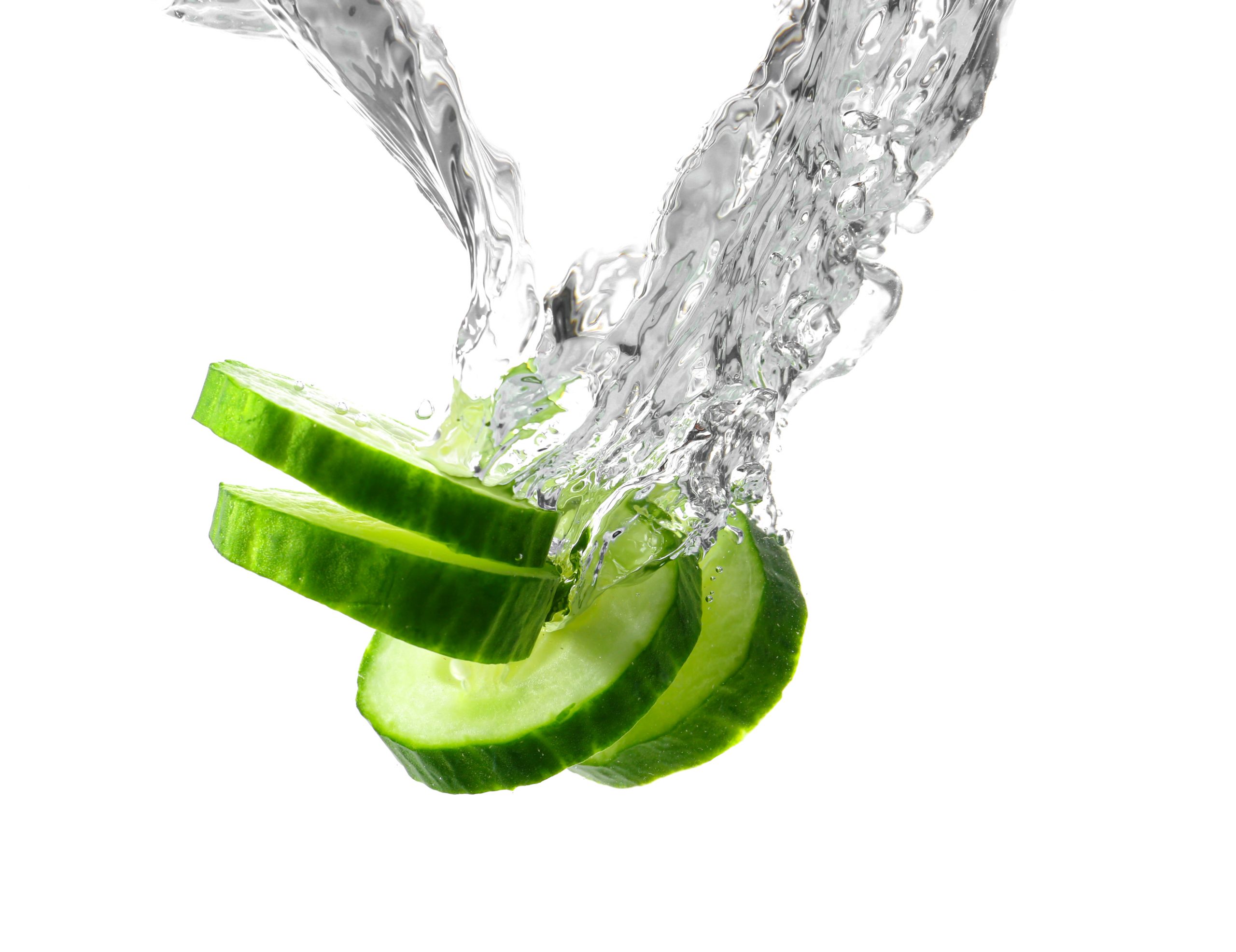 Falling of fresh cucumber slices into water against white background